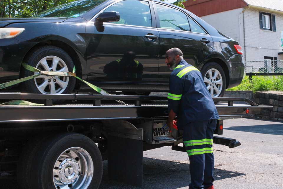 Tow truck driver loading black car onto flatbed tow truck