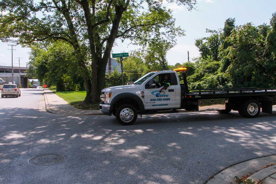 Elite Towing and Transporting truck drives down a residential street towards a broken down car